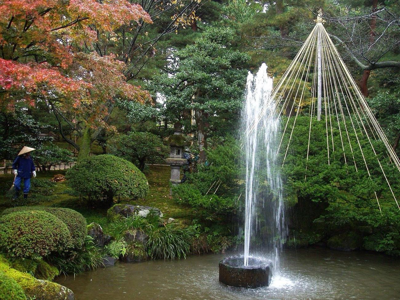 A pond and fountain amid manicured trees in Kenroku-en garden, Kanazawa